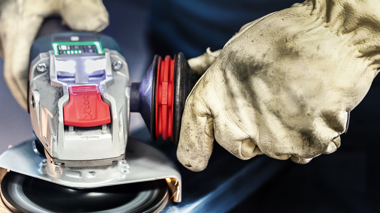 EXPERT Handle for Vibration Control M10 Angle Grinder 169 x 69 mm Person wearing safety equipment operates an angle grinder on a metal surface.