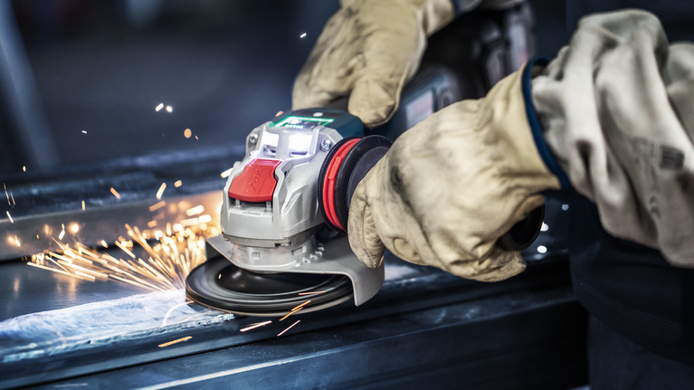 EXPERT Handle for Vibration Control M10 Angle Grinder 169 x 69 mm A person wearing safety equipment grinds metal, producing sparks.