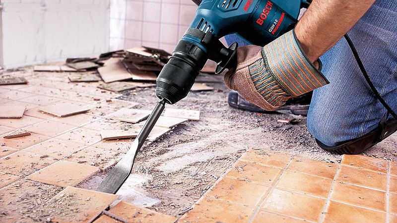 GSH 3 A person wearing safety equipment uses a demolition hammer to remove floor tiles.