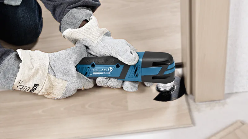 GOP 12V-28 A person wearing safety equipment trims a wooden floorboard with a cordless multi-cutter.