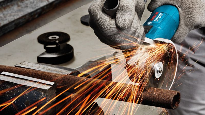 GWS 750 A person wearing safety equipment cuts a metal pipe with an angle grinder, sparks flying.