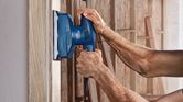 Person sands a wooden surface with an orbital sander.