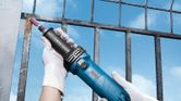 Person wearing safety equipment holds a blue straight grinder with a mounted abrasive tip.