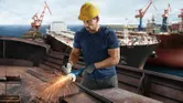 Worker grinding metal, shipyard.