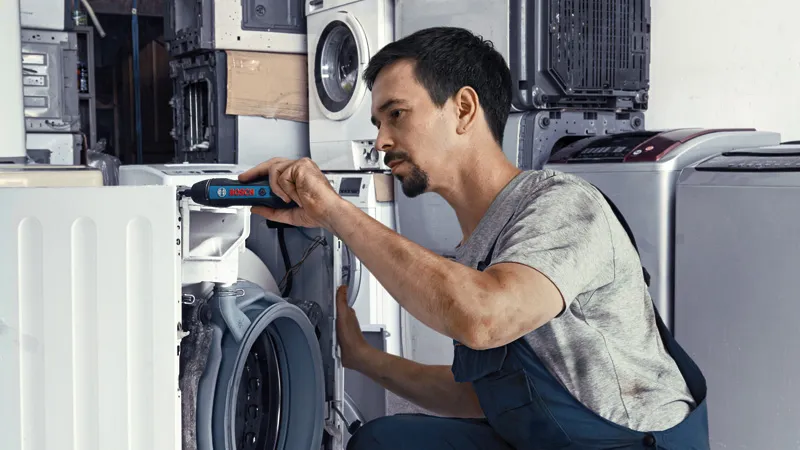 Bosch GO A person repairs a washing machine with a cordless screwdriver.