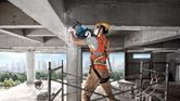 A person wearing safety equipment demolishes a concrete column using a demolition hammer.
