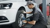 A person wearing safety equipment uses a cordless impact wrench to tighten wheel bolts on a car.