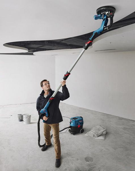 GTR 550 A person wearing safety equipment sands a ceiling with a drywall sander in a renovation space.