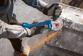 A person wearing safety equipment grinds concrete with a cordless angle grinder.