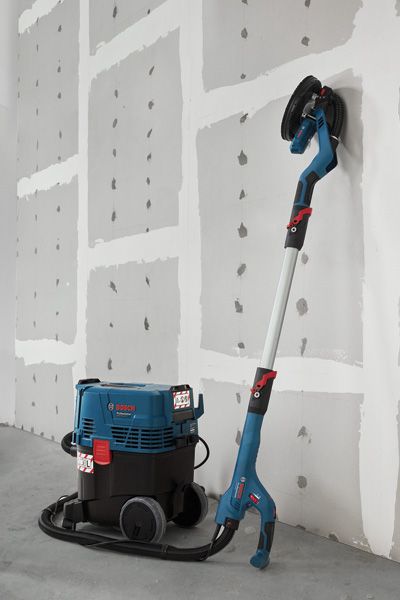 GTR 550 Drywall sander connected to a dust extractor standing against an unfinished wall.