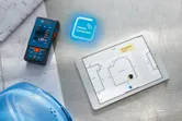 Laser measure next to blueprints and tablet displaying a digital floor plan.