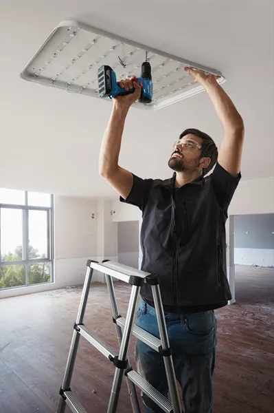 GSR 185-LI A person wearing safety equipment installs a ceiling light fixture using a power drill.