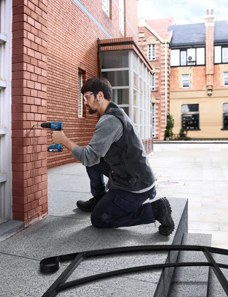 GSB 185-LI A person wearing safety equipment drills into a brick wall on a building exterior.
