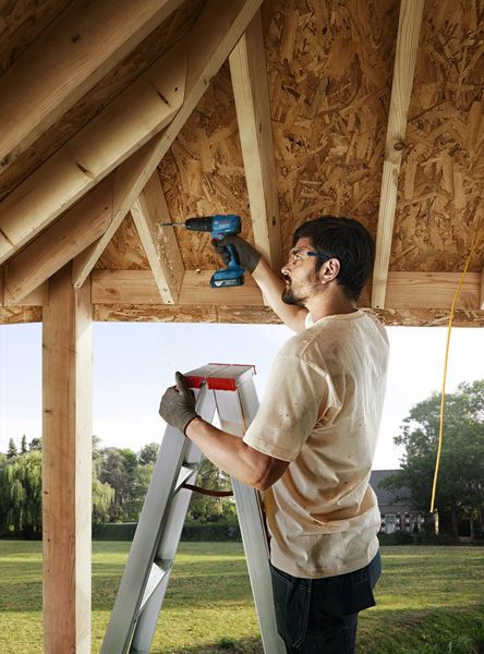 GSB 185-LI A person on a ladder drills into a wooden roof frame, wearing safety equipment.