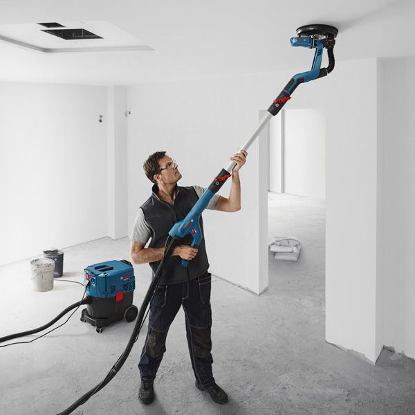 GTR 550 A person wearing safety equipment sands a ceiling with a drywall sander connected to a vacuum.