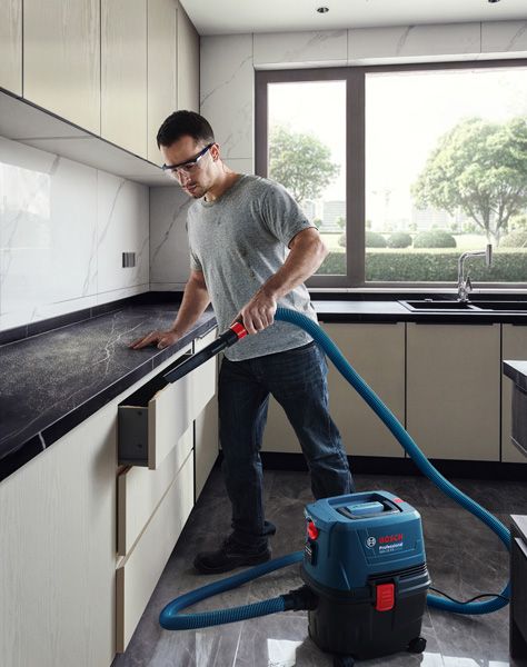 A person wearing safety equipment uses a wet dry extractor to clean kitchen surfaces.