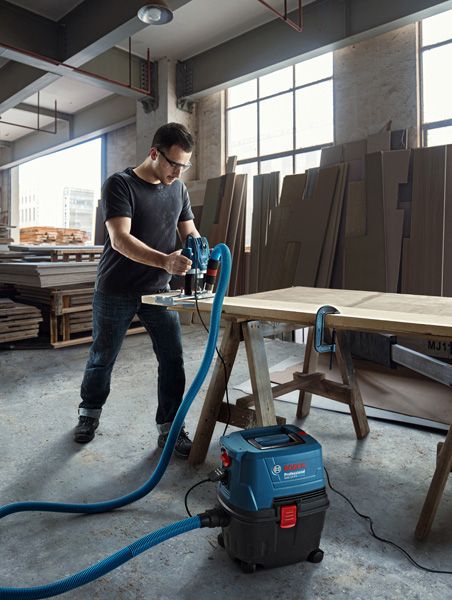A person uses a wet dry extractor connected to a power tool on a wooden table.