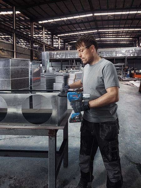 GRG 18V-16 C A person wearing safety equipment drills holes into metal air ducting in a factory.