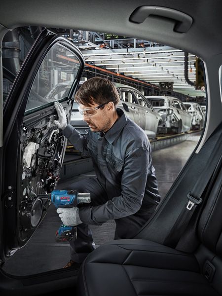 GRG 18V-16 C A person wearing safety equipment uses a power tool to assemble a car door in an automotive factory.