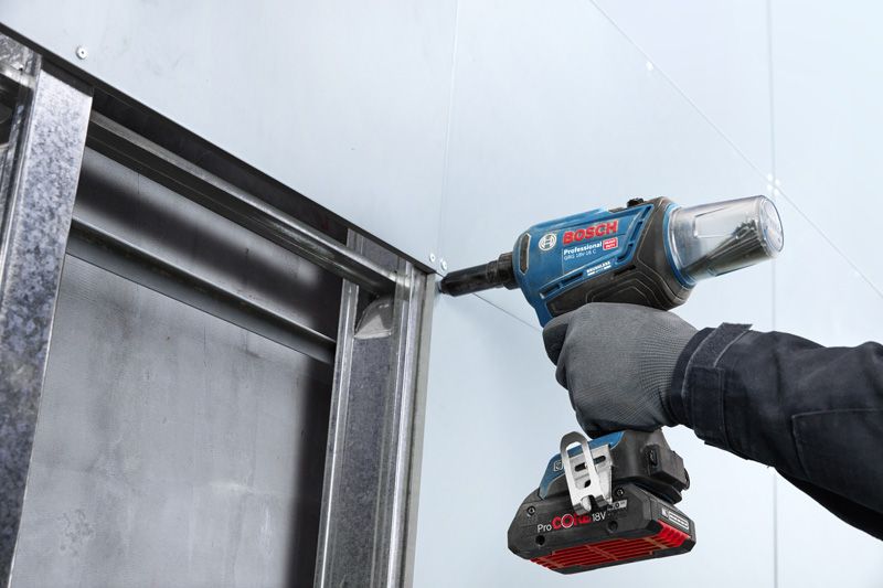 GRG 18V-16 C A person wearing safety equipment fastens drywall to a metal frame with a power tool.