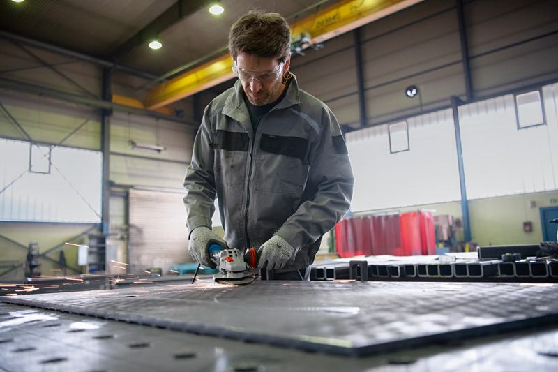 A person wearing safety equipment grinds a metal surface, creating sparks in a workshop.