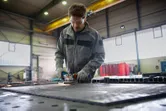 A person wearing safety equipment grinds a metal surface, creating sparks in a workshop.