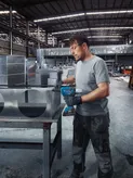 A person wearing safety equipment secures metal ductwork using a cordless rivet gun.
