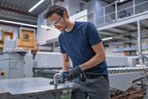 A person wearing safety equipment cuts sheet metal with a cordless metal shear.