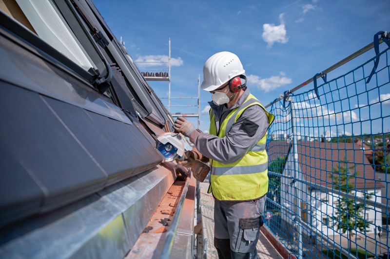 GWS 18V-180 P A person wearing safety equipment uses a cordless angle grinder on a building roof.