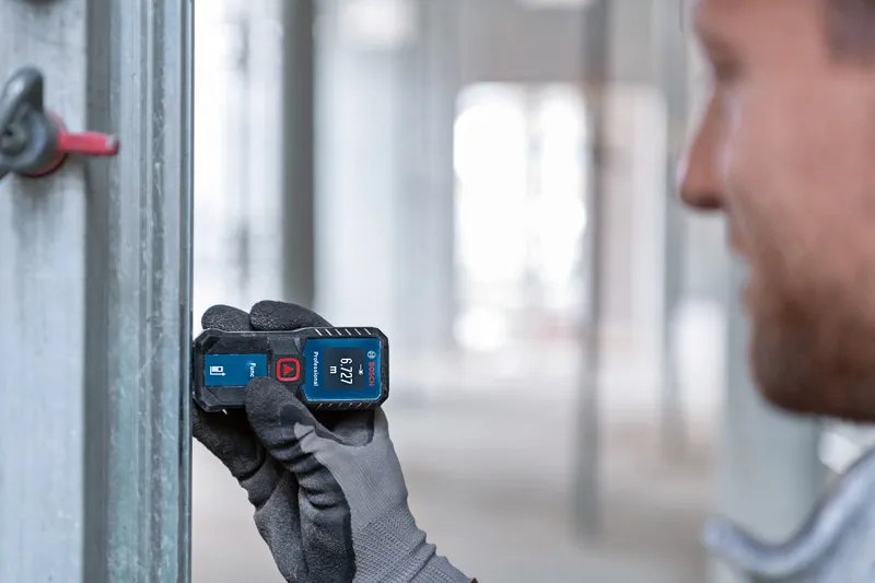 GLM 30-23 Person wearing safety equipment uses a laser measure to check distance on a metal beam.