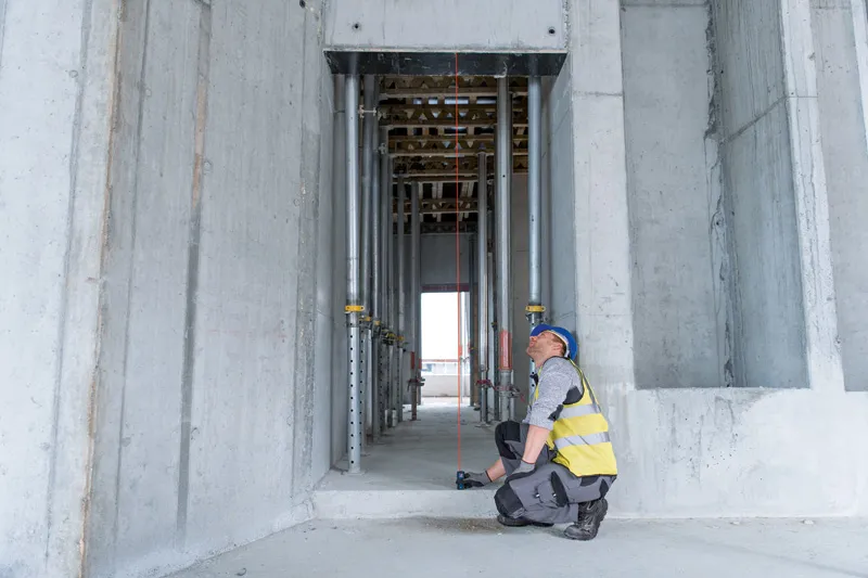 GLM 30-23 A person wearing safety equipment uses a laser measure to check distance in a concrete structure.