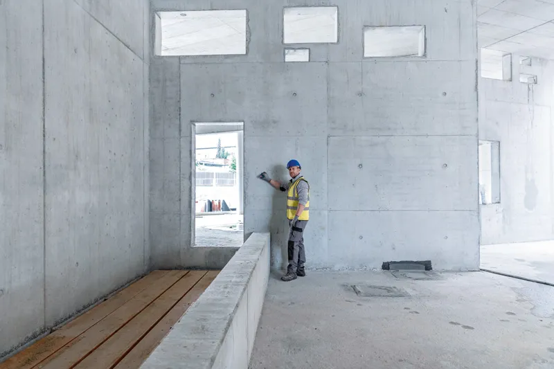 GLM 30-23 A person wearing safety equipment uses a laser measure against a concrete wall.