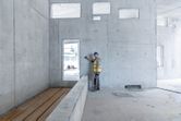 A person wearing safety equipment uses a laser measure against a concrete wall.