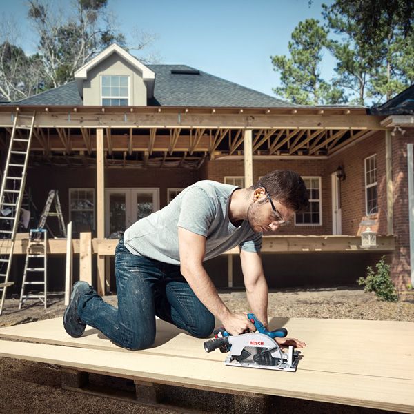 GKS 185-LI A person wearing safety equipment cuts wood with a cordless circular saw at a house construction site.
