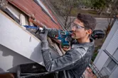 A person wearing safety equipment uses a reciprocating saw to cut wood on a rooftop.