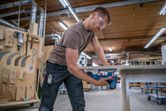A person wearing safety equipment cuts a wooden board with a power saw in a workshop.