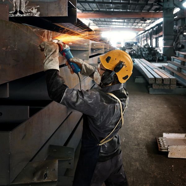 GWS 12-125 S A person wearing safety equipment grinds a metal beam, creating bright sparks.