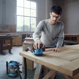 A person wearing safety equipment sands a wooden door with a connected orbital sander.