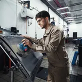 A person wearing safety equipment sands a car door with a power sander.