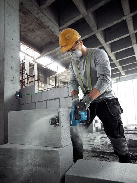 A person wearing safety equipment cuts an AAC block with a power cutter in a construction site.