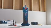 Cordless drywall router standing upright on a table next to its accessories and a pencil.