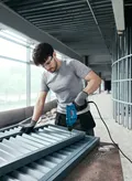Person wearing safety equipment drills screws into a metal frame on a construction site.