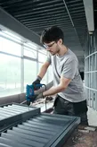 A person wearing safety equipment uses a power drill to assemble metal framing.