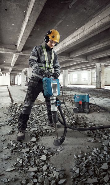 A person wearing safety equipment uses a breaker to demolish concrete flooring.