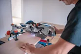 A person uses a cordless mitre saw with a laser leveling tool to cut wood.