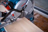 Cordless mitre saw cutting a wooden board with a laser leveling tool.