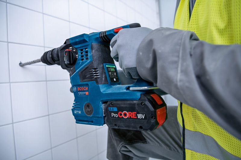 GBH 18V-28 CF A person wearing safety equipment drills into a tiled wall with a cordless rotary hammer.