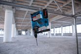 Cordless rotary hammer hanging on a metal pipe at an unfinished construction site.