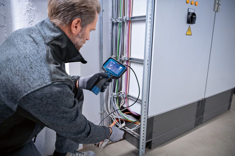 A person wearing safety equipment inspects electrical cables using an inspection camera.