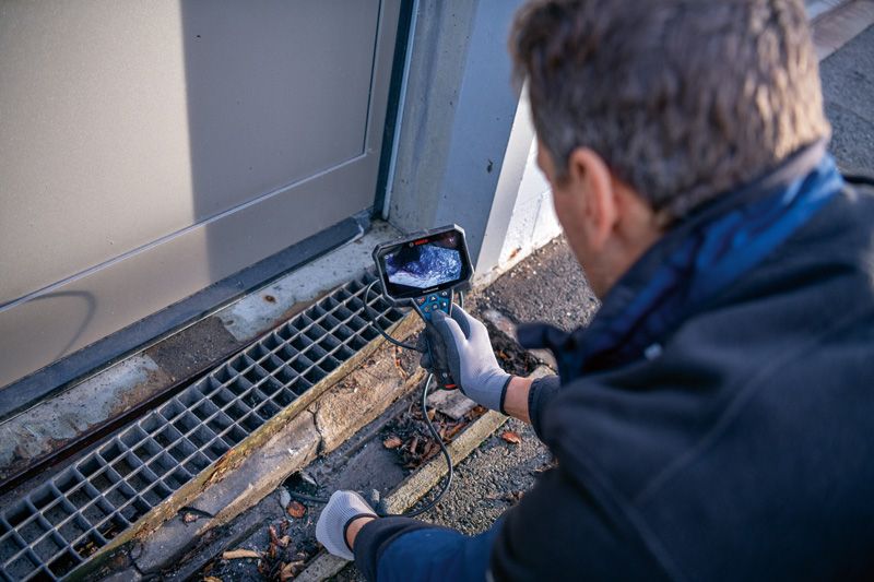GIC 5-27 C Person wearing safety equipment uses an inspection camera to examine a drain.